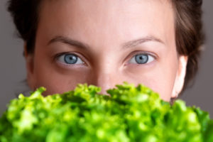Young adult beautiful caucasian happy smiling woman portrait holding green fresh lettuce salad crop in front face. Healthy food and nutrition concept. Green oraganic eco bio natural vegan meal.